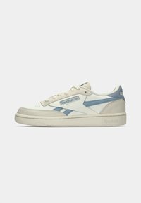 Niske Reebok tenisice u krem boji s plavim akcentima, vezicama i brend logotipom s prednje i stražnje strane, prikazane na bijeloj pozadini.