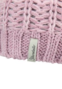 Close-up of pink knitted fabric with cable pattern and a white rectangular label sewn on, featuring cursive text.