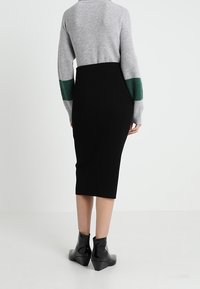 Pull gris à côtes avec des accents verts, associé à une jupe midi noire à côtes. Modèle portant des bottines noires. Vue de dos.