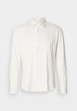 Wit shirt met lange mouwen gemaakt van zachte stof, voorzien van een knoopsluiting aan de kraag en een geborduurd logo op de borst. Soepele textuur, klassiek ontwerp.