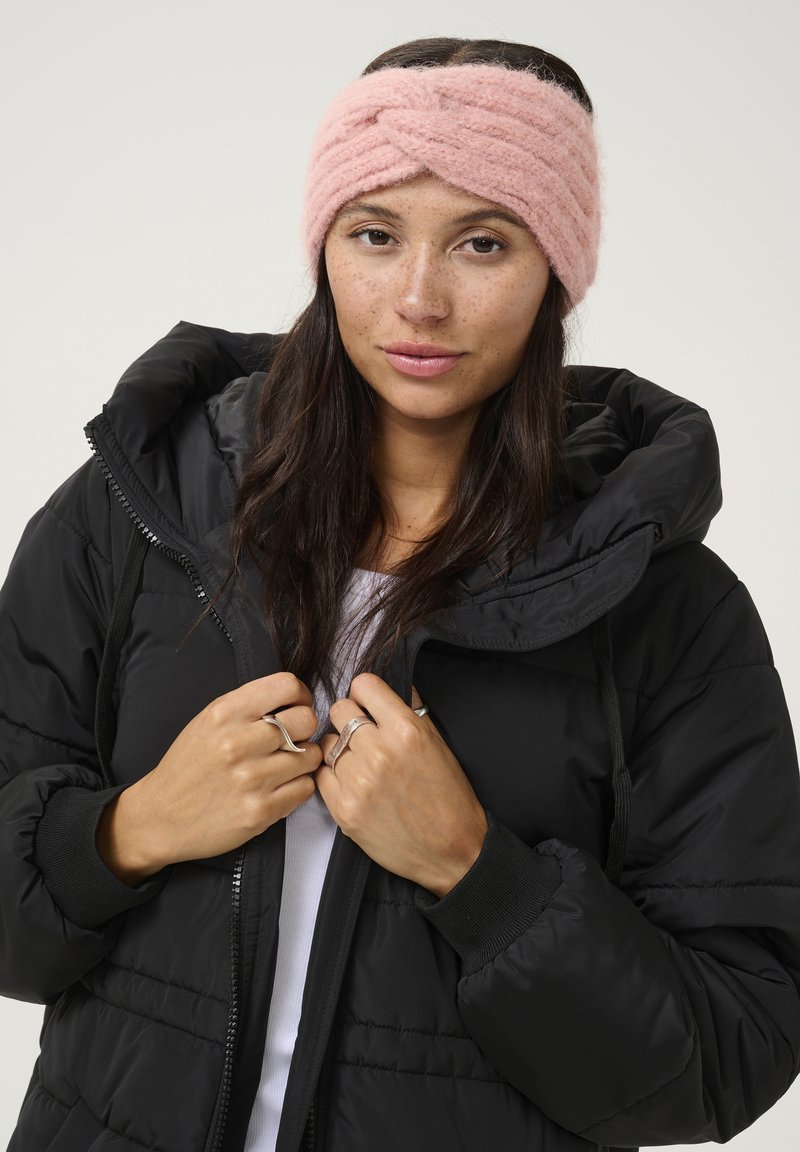 Rosa geflochtenes Haarband mit gedrehtem Design, kombiniert mit einer schwarzen Steppjacke. Die Jacke verfügt über einen Reißverschluss und gerippte Bündchen.