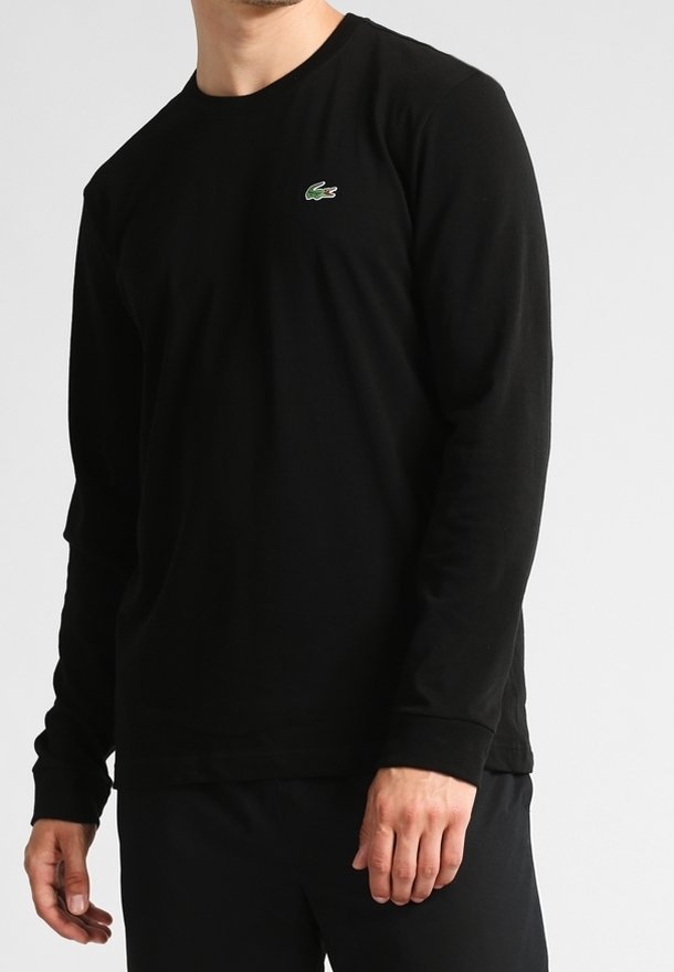 Black long-sleeve t-shirt with crew neck, made of cotton. Features a small green Lacoste logo on the chest. Smooth texture.