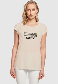 Light beige short-sleeve t-shirt with rounded neckline. Text printed in black: motivational quotes, including "IT'S NEVER TOO LATE" and "HAPPY."