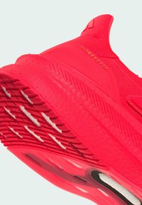 Helle rote Laufsohle mit strukturiertem Profil, "Ultraboost"-Markierung an der Ferse und einem sockenähnlichen Strickoberteil.