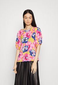 Blusa floral com mangas bufantes em rosa brilhante, azul e amarelo. Apresenta um decote arredondado e um corte descontraído, combinada com uma saia preta plissada.