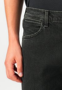 Zwarte denim jeans met een klassiek ontwerp, voorzien van vijf zakken, riemlussen en zichtbare stiksel-details. De textuur is glad met een lichte vervaging.