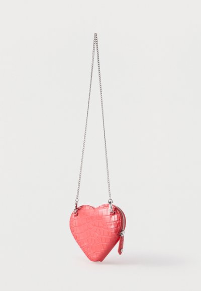 Κόκκινο πορτοφόλι σε σχήμα καρδιάς με υφή κροκόδειλου και ασημένια αλυσίδα, κλείσιμο με φερμουάρ στην πλευρά, κρεμασμένο μπροστά σε λευκό φόντο.