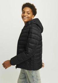 Zwarte pufferjack met capuchon, ritssluiting en gestikt padding. Gladde textuur met een slim fit. Beschikt over een logo patch op de mouw.