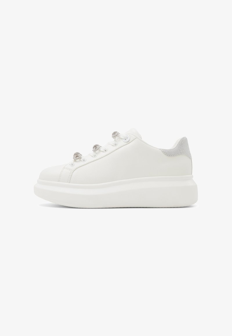 Zapatilla deportiva de plataforma blanca con lengüeta de tacón en glitter plata y ojales decorativos adornados con cristales, mostrada de perfil sobre un fondo blanco.