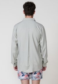 Lichtgrijs langslijfshirt met een relaxte fit, voorzien van een spitse kraag en een enkele rugpanddetail, gecombineerd met bloemen zwembroek.