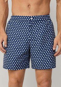 Marineblaue Schwimmshorts mit weißen Punkten, elastischem Bund mit Knopfverschluss, aus leichtem Stoff gefertigt, gerade geschnitten bis zum Saum.