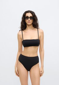 Μαύρο μπικίνι σετ με τοπ μπαντό με λεπτές τιράντες και σλιπ με ψηλή μέση. Λείο ύφασμα, μινιμαλιστικός σχεδιασμός και μονόχρωμο.