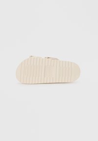 Suola di sandali beige chiaro con superficie texturizzata, caratterizzata da scanalature orizzontali e verticali per una migliore aderenza, progettata per comfort e stabilità.