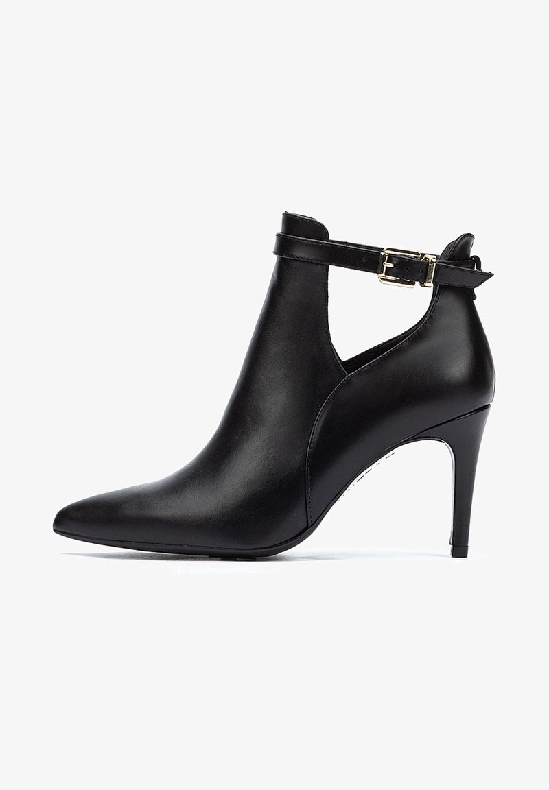 Botín de cuero negro hasta el tobillo con punta afilada, tacón alto de aguja y una correa ajustable con una hebilla dorada. Textura suave y diseño elegante.