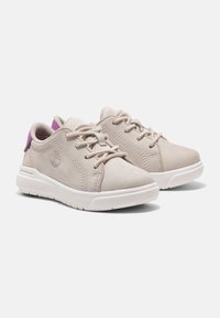 Beiga sneakers med ovandel av slätt läder, nätaccent, runda snörningar och en vit gummisula. Har en lila hälflik och logodetalj.