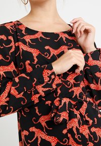 Schwarzes Kleid aus Stoff mit rotem Leopardenmuster, quadratischem Ausschnitt und langen Ärmeln mit geknöpften Manschetten, gebundenem Taillendetail.