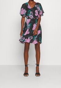 Robe noire à motifs floraux avec des fleurs roses et teal, manches évasées et décolleté en V. Tissu léger avec une jupe fluide et un ourlet volanté.