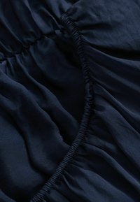 Gros plan sur un tissu bleu foncé avec des bords élastiques froncés créant des plis doux et une texture.