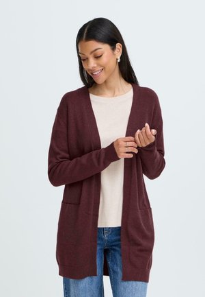 Burgunderfarbener Cardigan mit offenem Vorderteil, gestrickter Textur, langen Ärmeln und Seitentaschen, getragen über einem hellbeigen, gerippten Oberteil und blauen Jeans.