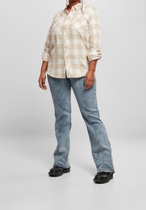 Beige en witte geblokte button-up shirt met opgerolde mouwen en een borstzak, gecombineerd met lichtblauwe jeans en zwarte enkellaarzen.