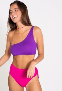 Top de bikini morado de un solo hombro combinado con braguitas de bikini rosadas de talle alto. Textura suave y colores sólidos, con un detalle de lazo en los laterales de las braguitas.