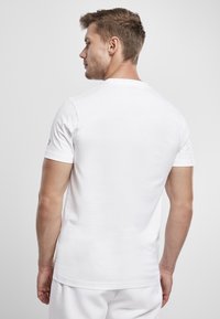 White short-sleeve t-shirt made of smooth fabric, featuring a crew neckline and minimal branding on the left sleeve. Clean, simple design.