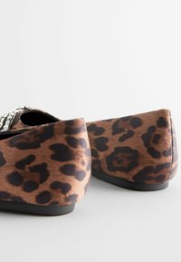Schuhe mit Leopardenmuster aus weichem braunem Material, ausgestattet mit einer schwarzen Sohle und einem dekorativen Strass-Akzent an der Vorderseite.