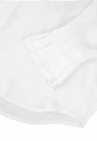 Hvit bluse med plisserte mansjett detaljer, glatt tekstur og avrundet kant. Stoffet virker lett og luftig.