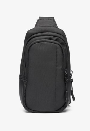 Compacte zwarte nylon schoudertas met twee ritsvakken en een gevoerde bovenriem, getoond tegen een witte achtergrond.