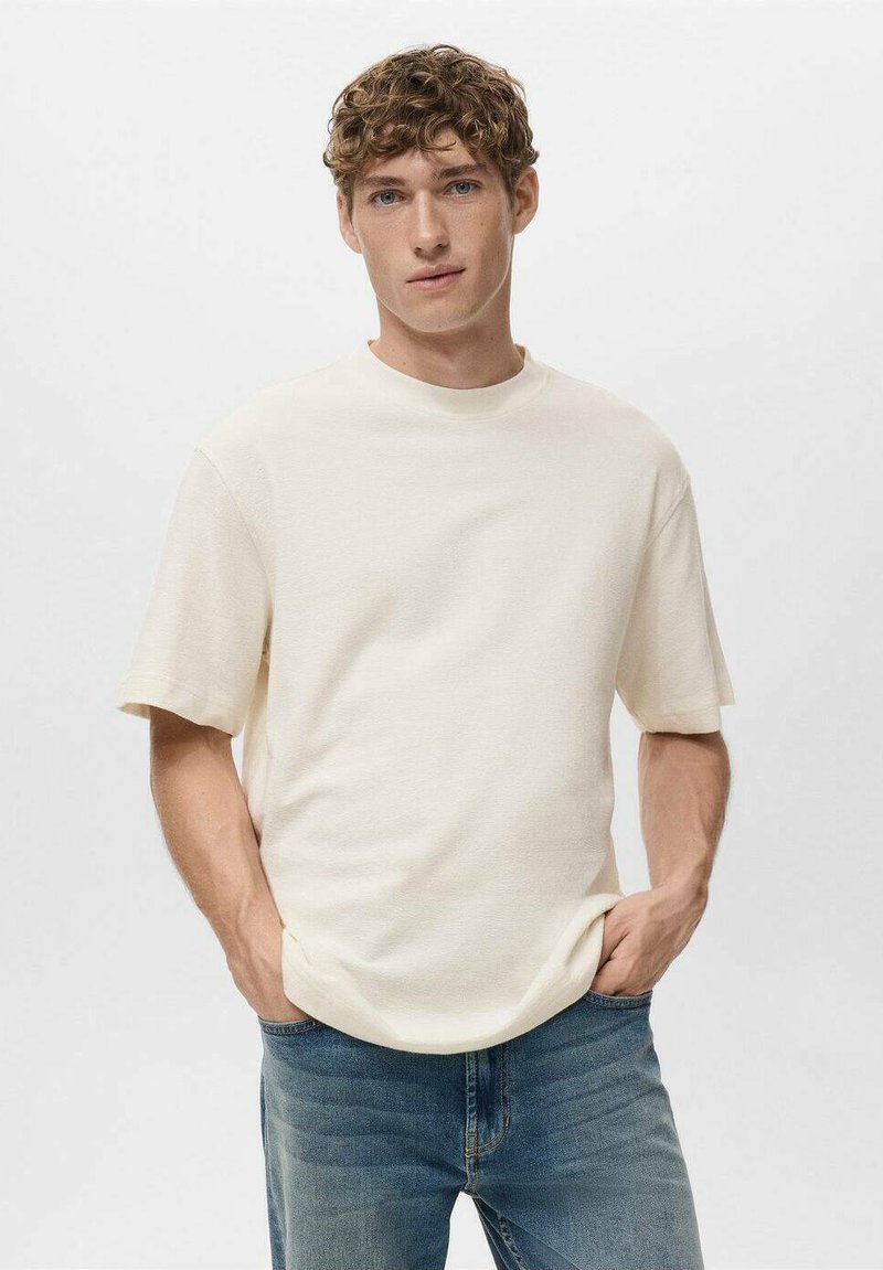 T-shirt color crema a maniche corte con scollatura tonda, realizzata in tessuto morbido. Abbinato a jeans blu, con una vestibilità rilassata.