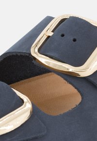Sandal in suede blu scuro con un design a taglio, dotata di una grande fibbia dorata come elemento hardware e di una soletta in pelle liscia color tan.