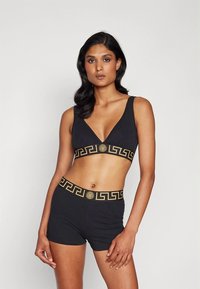 Conjunto desportivo preto com bralette e calções, com padrão dourado de chave grega na cintura, feito de material liso e elástico.