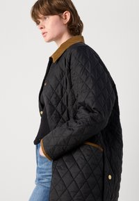 Quilted black jacket with a corduroy collar, featuring golden hardware and side pockets. Textured fabric with diamond pattern and contrast trim.