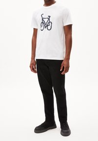 Vit bomulls-t-shirt med ett marinblått cykelmotiv, kombinerad med svarta byxor och svarta sneakers. Enkel design med rund hals och korta ärmar.