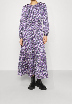 Robe fleurie violet avec des manches longues, un col froncé et une jupe en étages. Associée à des bottines noires.