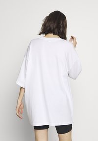 White oversized t-shirt in cotton, featuring dropped shoulders and short sleeves. Seam details and a relaxed fit enhance comfort.