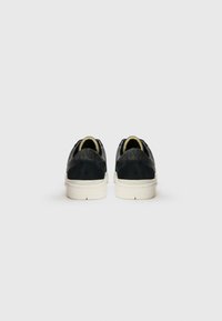 Black suede sneakers with a textured back, white soles, and a smooth finish. Subtle branding on the heel accent.