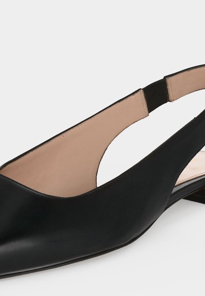Μαύρο δερμάτινο γυναικείο παπούτσι τύπου slingback με επίπεδη σόλα, μυτερή μύτη και μπεζ εσωτερική επένδυση σε λευκό φόντο.