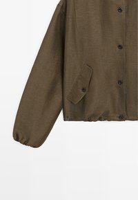 Bruine jas met knopen, lange elastische manchetten en een diagonaal genopte klepzak aan de linkerkant.