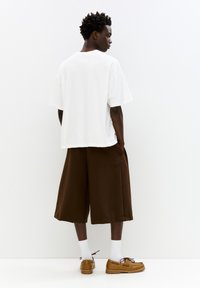 Hvid oversized t-shirt, brune knælange shorts, brune fodtøjet med snørebånd og hvide strømper. Enkelt, afslappet design med kontrastfarver.