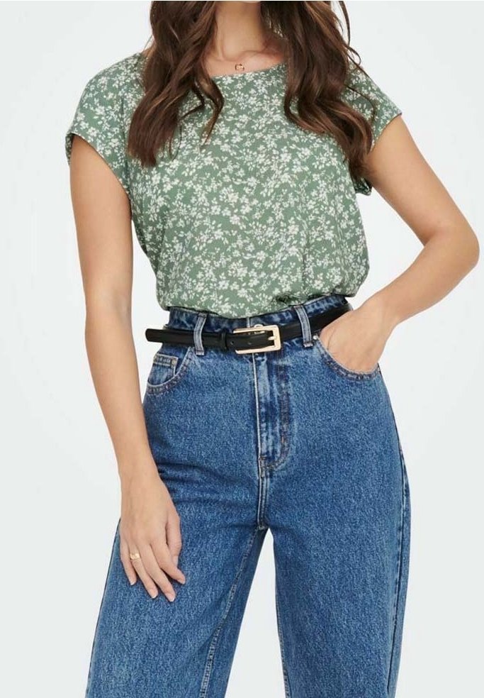 Femme portant un haut vert fleuri à manches courtes, rentré dans un jean bleu taille haute avec une ceinture noire et une boucle dorée.