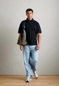 Černé polo tričko, světle modré volné džíny, šedé a bílé tenisky a zelená kabelka přes rameno. Jednoduchý design a funkční styl.
