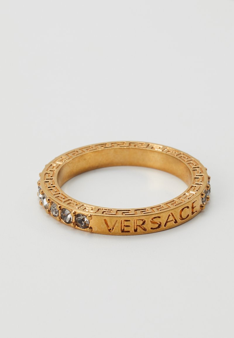 Bague couleur or gravée avec "VERSACE" et décorée de petites pierres transparentes ainsi que d'un motif géométrique sur la bordure.