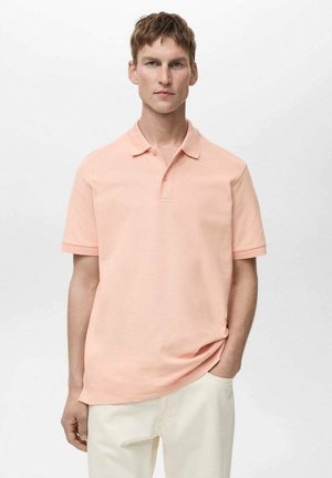 Ljust rosa kortärmad polo med krage och treknappsstängning, tillverkad av mjukt tyg, kombinerad med beige byxor.