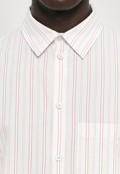Chemise blanche à manches longues avec de fines rayures rouges, un col classique et une poche sur le côté gauche de la poitrine. Les boutons sont blancs et équidistants.