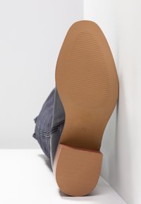 Svart ankelsko med en texturerad läderöverkropp, sned klack och en ribbad gummisula; storlek 37 markerad på undersidan.