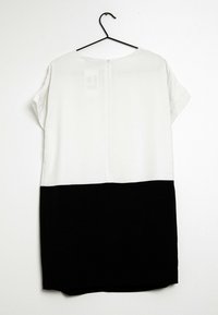 Hame dress lyhyillä hihoilla, jossa on valkoinen yläosa ja musta alaosa. Tasainen kangas, suora leikkaus, takana vetoketjukiinnitys.