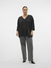 Haut noir à col en V avec des manches trois-quarts, associé à un jean large gris taille haute et des talons noirs à bout pointu. Texture lisse.