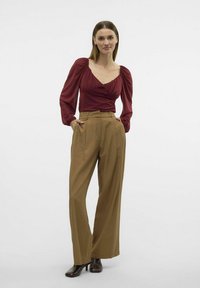 Blouse bordeaux à manches longues avec épaules froncées, associée à un pantalon taille haute à jambe large en kaki et des talons noirs. Couleurs unies, sans motifs.