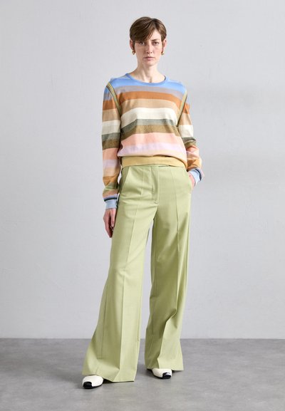 Striped knitted sweater in pastel colors, paired with high-waisted green wide-leg trousers and two-tone slip-on shoes.